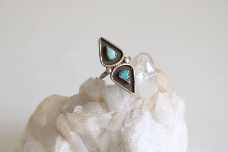 May include: A silver ring with two turquoise stones set in a triangular shape.