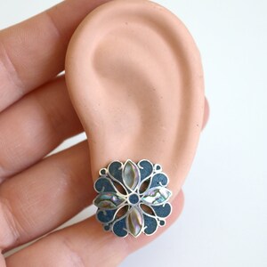 May include: A silver and abalone shell flower-shaped earring with a dark blue background.