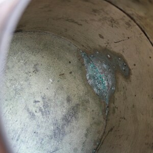 May include: Close-up of the interior of a weathered metal container. The aged surface shows a mix of brown and green hues, with visible signs of wear and oxidation. The container's interior has a textured, aged appearance.
