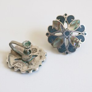 May include: A pair of silver clip-on earrings with a blue and iridescent abalone shell flower design. The earrings are marked "925 Mexico".