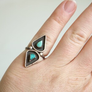 May include: A silver ring with two turquoise stones set in a geometric design.