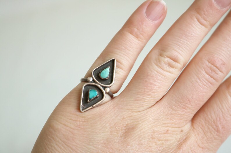 May include: A silver ring with two turquoise stones set in a geometric design.