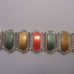 May include: A silver bracelet with alternating orange, green, and gold rectangular stones. The stones are set in a decorative silver frame.