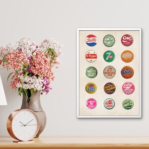 May include: A vintage-style print featuring 16 colorful soda bottle caps with various brand names, including Sprite, Coke, Dr Pepper, 7 Up, Mountain Dew, Fanta, and more. The print is on a cream-colored background and is framed in white.