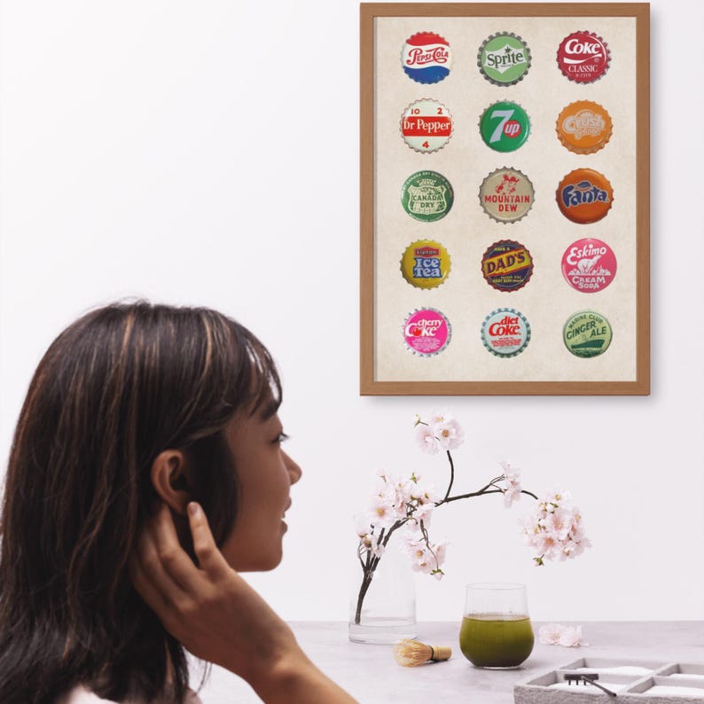 A framed print of vintage soda bottle caps. The caps are arranged in a grid of four rows and three columns. The caps are all different colors and feature various soda brands including Dr Pepper, 7 Up, Mountain Dew, Fanta, and Coke.