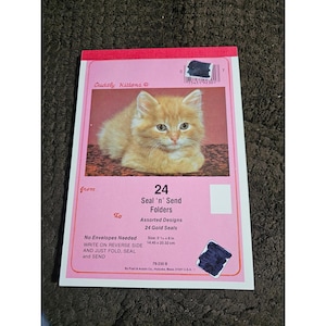 May include: A rectangular package of 24 Cuddly Kittens Seal 'n' Send Folders with a pink background and an orange kitten image. The text reads 24 Seal 'n' Send Folders, Assorted Designs, 24 Gold Seals, No Envelopes Needed, and size 5.75 x 8 inches.