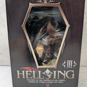 May include: A boxed Hellsing figure. The box is dark brown with a hexagonal window showing the figure inside. The Hellsing logo is at the bottom, with the text "The Bird of the Hermes is my name, eating my wings to make me tame."