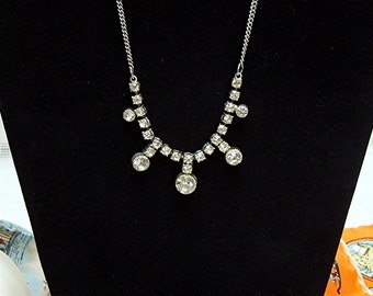 May include: A silver chain necklace with a cluster of clear rhinestones in a teardrop shape.