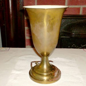 May include: A vintage brass chalice with a wide, flaring top and a pedestal base. The interior of the chalice is white, and the exterior has a tarnished, aged appearance. The chalice is likely used for religious ceremonies.