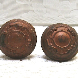 May include: Two antique door knobs with ornate designs. The knobs are made of a dark brown metal and have a worn, aged finish.