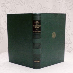 May include: A hardcover book titled "The World of Washington Irving" by Van Wyck Brooks. The book has a dark green cover with gold lettering and a gold emblem. The spine is a darker green with horizontal lines and the publisher's name, DUTTON.