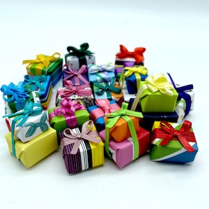 May include: A collection of miniature wrapped gifts in various colors, including yellow, green, pink, and blue. Each gift is tied with a matching or contrasting ribbon, creating a festive and colorful display. The gifts are arranged on a white surface.