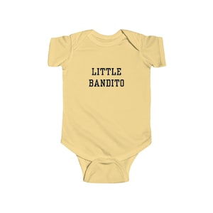 May include: A light yellow baby bodysuit with the text "LITTLE BANDITO" in black block letters. The bodysuit has short sleeves and a snap closure at the bottom.