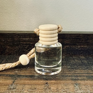 May include: A clear glass bottle with a wooden cap and a rope for hanging. The cap is made of stacked wooden rings. The bottle sits on a wooden surface. The rope has a wooden bead.