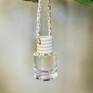 May include: A clear glass bottle with a white lid and a gold and white string hanging from it. The bottle contains a pink and green liquid with small, colorful pieces inside.