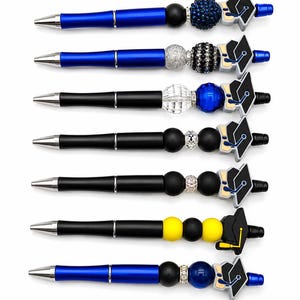 Peut inclure: Plusieurs stylos sur le thème de la remise de diplômes. Les stylos ont des corps noirs ou bleus avec des détails argentés. Chaque stylo est orné de perles décoratives et d'un charm en forme de toque de diplômé noir, blanc et jaune.