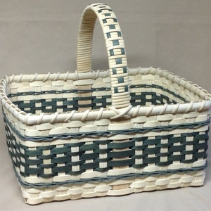 May include: A rectangular woven basket with a handle. The basket is made of natural colored and dark green reeds. The basket has a checkered pattern.