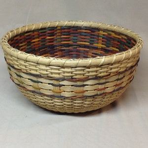 May include: A woven basket with a natural brown exterior and a colorful interior. The interior is woven with strips of brown, red, orange, yellow, green, and blue.