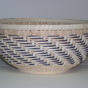 May include: A woven basket with a natural beige color and blue accents. The basket is round and has a wide opening. It is made of natural materials and has a traditional design.