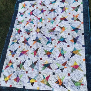 May include: A white quilt with a blue border featuring a patchwork design of colorful stars. The stars are made of various fabrics and colors, creating a vibrant and eye-catching pattern.