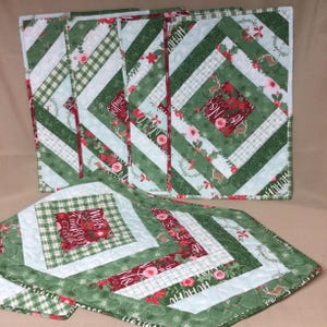 May include: Set of four green and white quilted placemats with a red and white plaid design and the text "Merry Christmas" and a green and white quilted table runner with a red and white plaid design and the text "Merry Christmas".