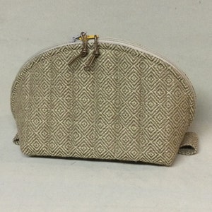 May include: A beige and brown fabric cosmetic bag with a zipper closure and a diamond pattern. The bag has a curved shape and a small handle.