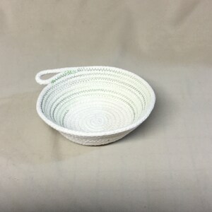 May include: White rope bowl with a green accent and a handle. The bowl is made of woven rope and has a circular shape.