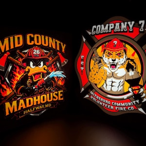 Puede incluir: Dos parches coloridos con temas de bomberos. Uno presenta un pato con uniforme de bombero con hachas y el texto "Mid County Madhouse". El otro muestra un guepardo musculoso con una manguera contra incendios y el texto "Company 7."