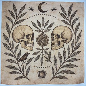 May include: A beige square print featuring two skulls facing each other, surrounded by botanical elements. A bird, a flower, a crescent moon, stars, and a sun are also depicted in the design. The artwork has a vintage, gothic aesthetic.