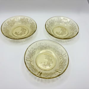 May include: Three yellow glass bowls with floral designs. The bowls have a shallow, rounded shape with a decorative floral pattern around the rim and center. The glass has a slightly translucent quality.