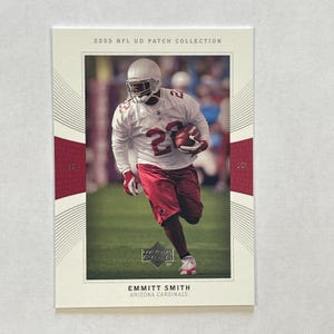May include: A 2003 NFL UD Patch Collection trading card featuring Emmitt Smith of the Arizona Cardinals. The card shows a player in a white jersey with the number 22 and red shorts, holding a football while running on a green field.
