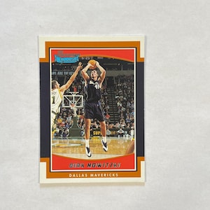 May include: A Bowman Signature basketball trading card featuring Dirk Nowitzki in a Dallas Mavericks uniform, mid-jump shot on a court. The card has an orange and dark blue border with the text Dirk Nowitzki and Dallas Mavericks printed below.