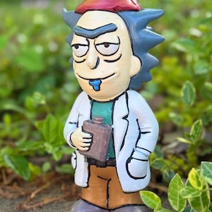 Peut inclure: Figurine de gnome de jardin fantaisiste représentant un personnage avec des cheveux bleus hérissés, un chapeau rouge et une blouse blanche. La figurine tient une fiole marron et a une bave bleue. Le gnome est devant un feuillage vert.
