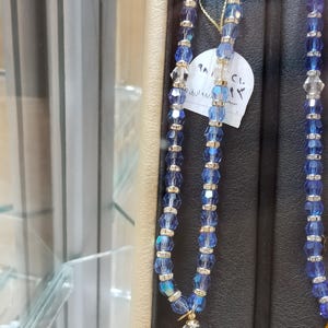 May include: A blue and silver crystal prayer beads with a gold tassel. The beads are strung on a thin string and have a small tag attached with the text "سعر ٩/٨/٢٠٢٣  ١٢٠  ريال"