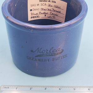 May include: A blue ceramic butter crock with the text "Morlea Brand Creamery Butter." The crock has a cylindrical shape and is approximately 4 inches in diameter. A label on the side reads "Blue Butter Crock."
