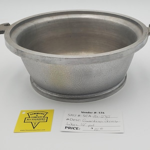 May include: A round, silver-colored metal pot with two side handles and a textured exterior finish. The pot is accompanied by a yellow auction tag and a white card labeled Vendor #: 534, SKU #: SCA-26-595, and Guardian Service Ware 10" pot.