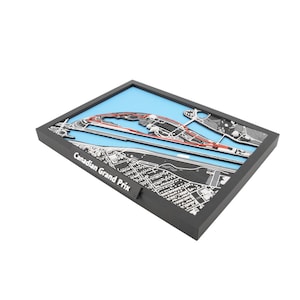 May include: A framed, three-dimensional map of the Canadian Grand Prix race track. The track is highlighted in red against a blue background, with surrounding infrastructure in black and white. The frame is black, and the text "Canadian Grand Prix" is visible on the side.