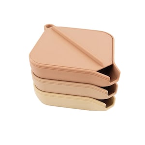 May include: Three stacked, beige-colored, leather-like trays. The top tray is a light peach color, with a raised ridge and a small opening on one side. The other two trays are a lighter shade of beige.