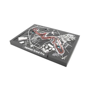 May include: A dark gray, rectangular relief map of the Japanese Grand Prix race track. The track is highlighted in red, with white lines indicating roads and buildings. The text "Japanese Grand Prix" is printed on the front.