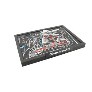 May include: A detailed, three-dimensional model of the Chinese Grand Prix race track. The track is rendered in red, white, and black, with the words "Chinese Grand Prix" printed on the frame. The model is set in a black frame.