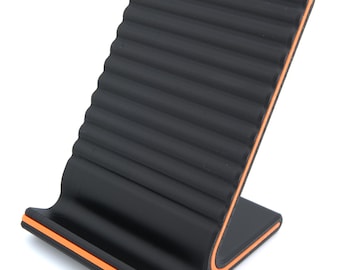 May include: A black phone stand with a ridged surface and orange trim. The stand is designed to hold a phone or tablet at an angle for easy viewing. The stand is made of a durable material and is suitable for home or office use.