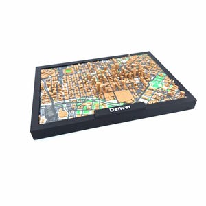 May include: A 3D map of Denver, Colorado, featuring a detailed representation of the city's layout. The map is in shades of brown and green, with a black frame and the city name displayed in white. The map is a unique decorative item.