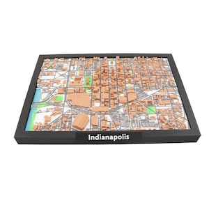 May include: A 3D map of Indianapolis, Indiana, in a black frame. The map features detailed representations of buildings, roads, and green spaces. The city name "Indianapolis" is printed on a black label at the bottom.