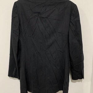 May include: A dark gray blazer with a subtle pinstripe pattern. The blazer has a notched lapel, long sleeves, and three buttons on each cuff. The back of the blazer is visible, showing the tailored fit and the fabric's texture. A classic piece of formal wear.