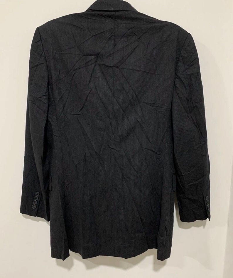 May include: A dark gray blazer with a subtle pinstripe pattern. The blazer has a notched lapel, long sleeves, and three buttons on each cuff. The back of the blazer is visible, showing the tailored fit and the fabric's texture. A classic piece of formal wear.