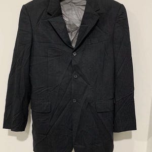 May include: A black blazer with a three-button closure, two front pockets, and a notched lapel. The blazer is made of a textured fabric and is hanging on a black hanger.