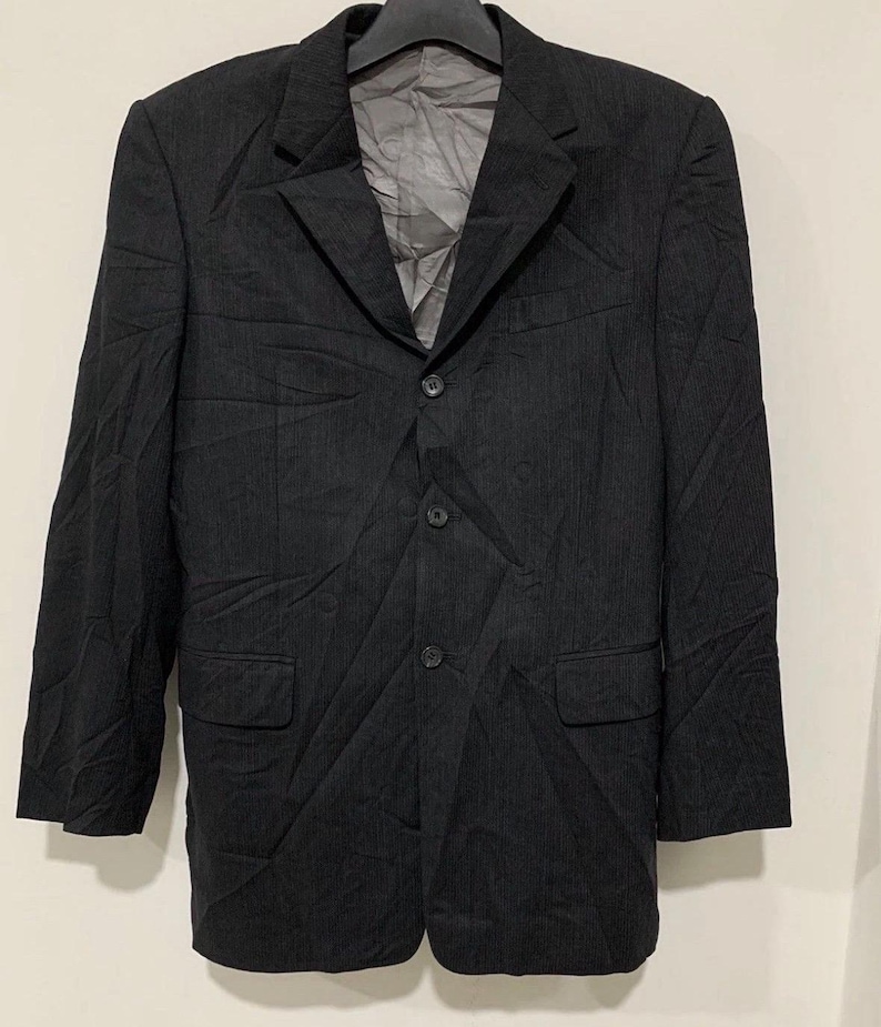 May include: A black blazer with a three-button closure, two front pockets, and a notched lapel. The blazer is made of a textured fabric and is hanging on a black hanger.