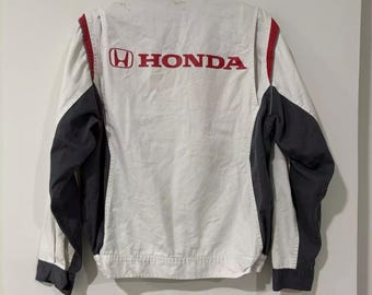 May include: White and gray jacket with the red "HONDA" logo on the back. The jacket has a black collar and sleeves, with red accents along the shoulders. The jacket is hanging on a metal hanger.