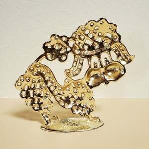 Op de afbeelding: Gouden metalen decoratieve standaard met een boomontwerp. De standaard heeft een ronde basis en is gemaakt van ingewikkeld, opengewerkt metaal. De tekst "REVERE WARE" is zichtbaar op de standaard.