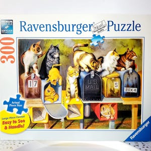 May include: Ravensburger 300-piece jigsaw puzzle featuring a whimsical scene of cats perched on and in mailboxes. The puzzle box has the Ravensburger logo and text that reads "Large Piece Format Easy to See & Handle!"
